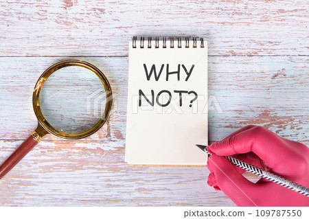 WHY NOTwriting on a notebook lying on old boards next to a magnifying glass and a hand in a red medical glove with a pencil 109787550