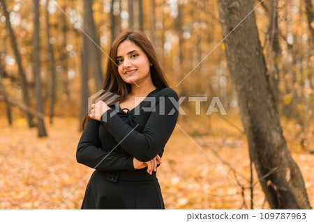 Close-up portrait of diversity young beautiful confident Indian Asian woman in black dress in fall outdoor copy space mockup. Happy and natural smiling female. Generation z and gen z youth concept 109787963