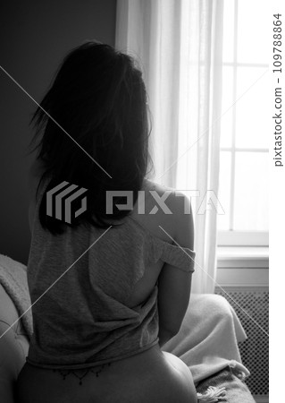 portrait on back view of woman wearing a sexy tee-shirt sitting on sofa looking at the window in black and white 109788864