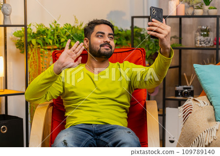 Happy Indian man taking selfie on smartphone communicating video call home online with subscribers Happy Indian man taking selfie on smartphone communicating video call home online with subscribers 109789140