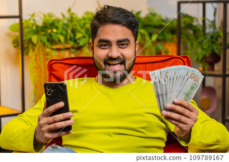 Rich happy Indian man counting money cash on smartphone calculator app, calculate income earnings Rich happy Indian man counting money cash on smartphone calculator app, calculate income earnings 109789167
