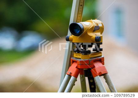 Yellow theodolite on a tripod and a ruler with a blurred background. Geodetic measurements. 109789529