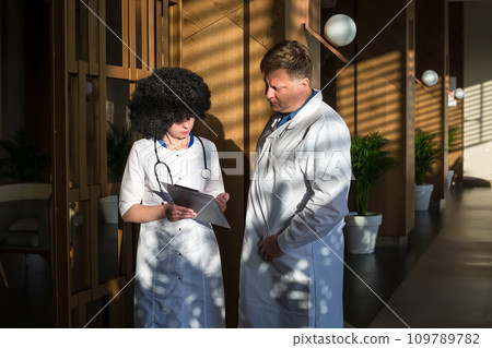 Two doctors, a man and a woman, are having a discussion in the corridor of a clinic Two doctors, a man and a woman, are having a discussion in the corridor of a clinic 109789782