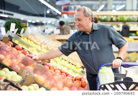 Elderly man chooses apples in vegetable and fruit department Elderly man chooses apples in vegetable and fruit department 109790693