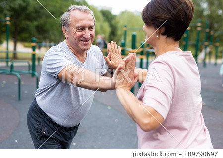 Elderly man and a woman are doing gymnastics on an open-air sports ground Elderly man and a woman are doing gymnastics on an open-air sports ground 109790697