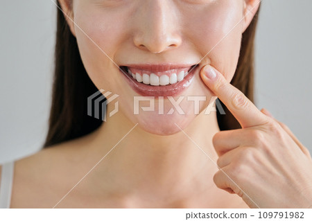 A woman in her 30s with white teeth pointing at her mouth 109791982