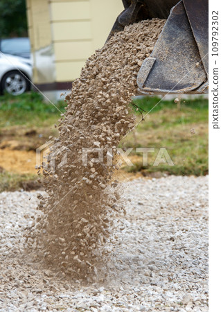 a bulldozer pours macadam from a bucket onto the ground at a construction site - close-up view a bulldozer pours macadam from a bucket onto the ground at a construction site - close-up view 109792302