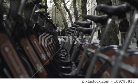Close-up of bicycles standing on the street and walking people. Action. Bicycles are available to hire at various locations around London Close-up of bicycles standing on the street and walking people. Action. Bicycles are available to hire at various locations around London 109793935