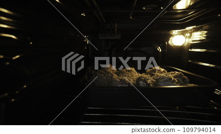 Close up of raw chicken under the cheese in the oven. Action. Meat of chicken under the sauce and cheese being baked in the oven, concept of food and cooking. 109794014