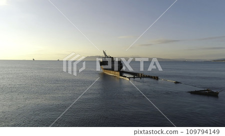 View of a old sunken ship on a shoal in sea against the sunset sky and mountains. Shot. Old seagoing vessel 109794149
