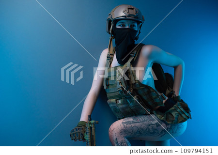 sexy girl soldier in a helmet, armed with an automatic rifle, in military clothes on a blue background 109794151