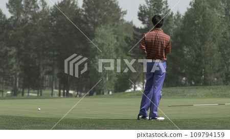 Golfer Hitting Ball with Club on Beautiful Golf Course. Golfer hits an fairway shot towards the club house. Man hitting driver on a golf course in the sun. Professional male golf player 109794159