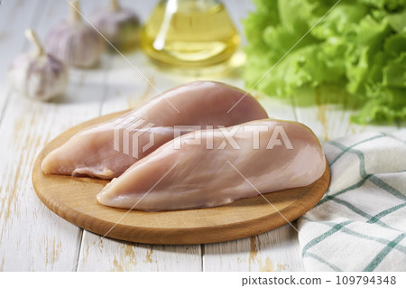 Raw chicken breast with salt, garlic and fresh herbs on a white table. Healthy food. Raw chicken breast with salt, garlic and fresh herbs on a white table. Healthy food. 109794348