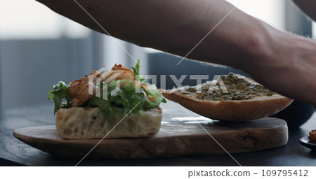 man making ciabatta sandwich with shrimps, olives and pesto man making ciabatta sandwich with shrimps, olives and pesto 109795412