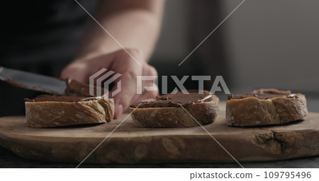man spreading chocolate hazelnut spread on ciabatta slice on wood board man spreading chocolate hazelnut spread on ciabatta slice on wood board 109795496