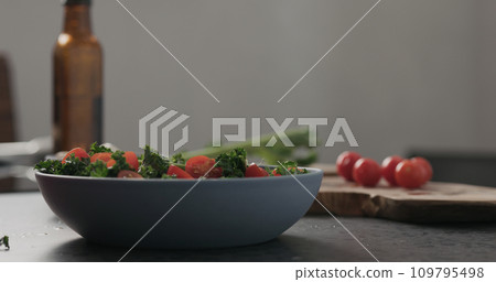 Slow motion man hands put tomatoes on top of kale in blue bowl on concrete surface 109795498