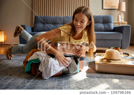 Excited woman preparing travel suitcase at home trying to close full suitcase 109796166
