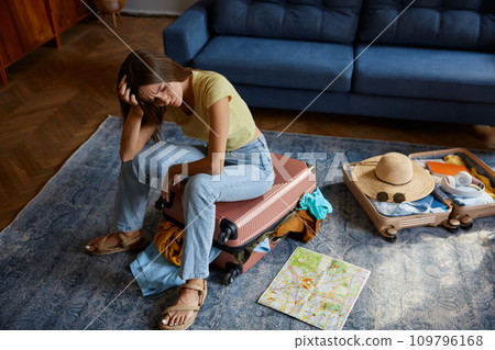 Frustrated young woman sitting on travel suitcase with clothes excess 109796168
