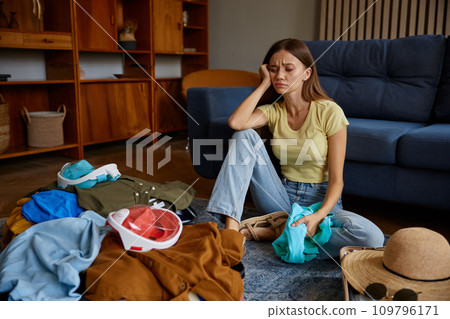 Troubled young woman preparing luggage for travel at home Troubled young woman preparing luggage for travel at home 109796171