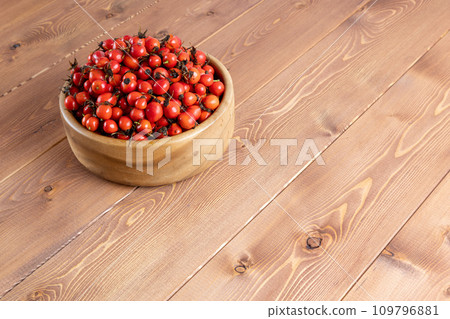 red dog-rose rosehip fruits in a wooden bowl on wooden table 109796881