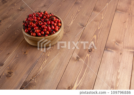 red dog-rose rosehip fruits in a wooden bowl on wooden table 109796886