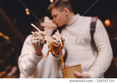 newlywed couple eating noodles with chopsticks in Shanghai outside a food market near Yuyuan. Couple eating authentic local food. husband and wife eating chinese food outisde of a food hall newlywed couple eating noodles with chopsticks in Shanghai outside a food market near Yuyuan. Couple eating authentic local food. husband and wife eating chinese food outisde of a food hall 109797154