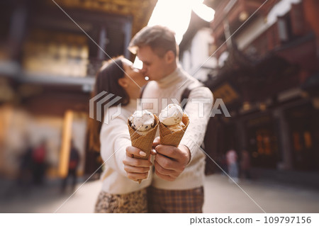 newlywed couple eating ice cream from a cone on a street in Shanghai near Yuyuan. Couple take a break for a snack while visiting China. husband and wife sharing ice cream outisde of a food hall 109797156
