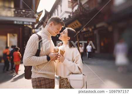 newlywed couple eating ice cream from a cone on a street in Shanghai near Yuyuan. Couple take a break for a snack while visiting China. husband and wife sharing ice cream outisde of a food hall newlywed couple eating ice cream from a cone on a street in Shanghai near Yuyuan. Couple take a break for a snack while visiting China. husband and wife sharing ice cream outisde of a food hall 109797157