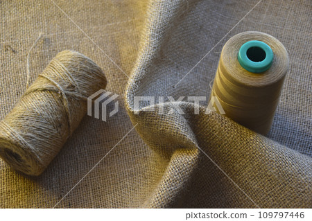 Skeins of thread on crumpled burlap. Yellow threads on coarse cloth. The material for the bags. Skeins of thread on crumpled burlap. Yellow threads on coarse cloth. The material for the bags. 109797446