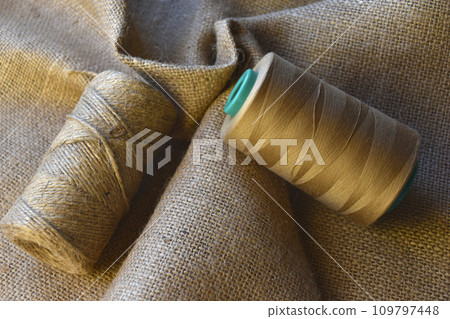 Skeins of thread on crumpled burlap. Yellow threads on coarse cloth. The material for the bags. 109797448