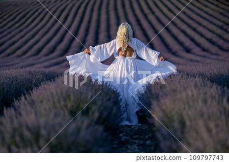 Blonde woman poses in lavender field at sunset. Happy woman in white dress holds lavender bouquet. Aromatherapy concept, lavender oil, photo session in lavender 109797743