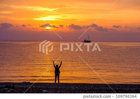 Lonely woman waving to the yacht in the sea at sunrise Lonely woman waving to the yacht in the sea at sunrise 109798164
