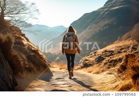 a woman is walking on a path near a mountain in the mountains a woman is walking on a path near a mountain in the mountains 109799568