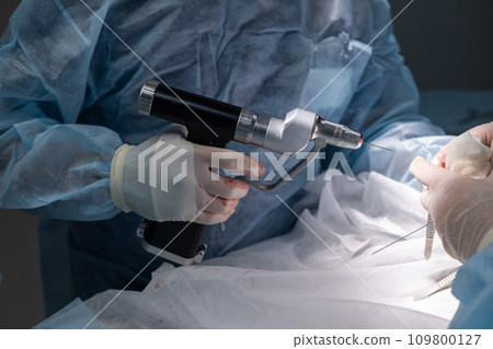 A veterinary surgeon's hand holds a surgical drill and inserts a knitting needle into the broken bone of a pet's paw Orthopedic veterinary surgery to stabilize a broken bone in a pet. Osteosynthesis. 109800127