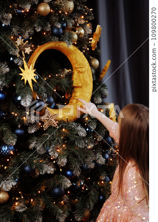 Girl in a dress decorates the Christmas tree at home Girl in a dress decorates the Christmas tree at home 109800270