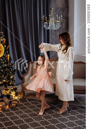 Mother and daughter dancing near a Christmas tree. 109800368