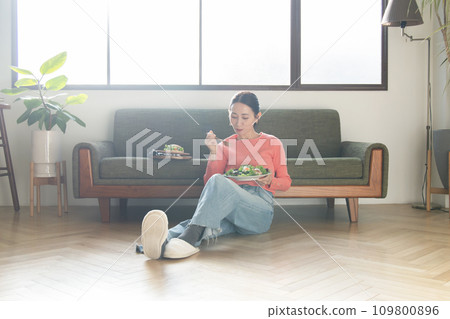 woman eating salad in the living room woman eating salad in the living room 109800896