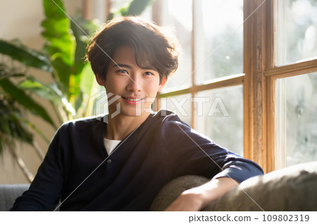 Young Asian man with curly hair smiling in backlight (AI generated image) 109802319