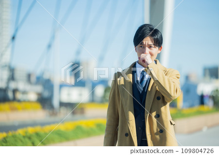 A young man in a suit walking through the city in winter, feeling unwell 109804726