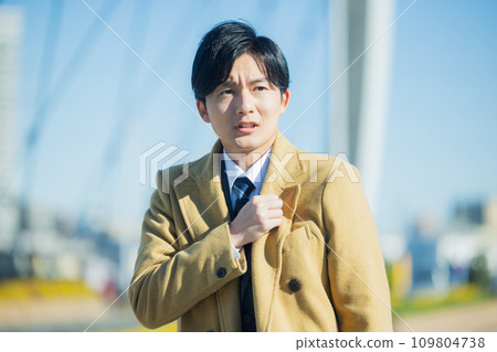 A young man in a suit walking through the city in winter, feeling unwell 109804738