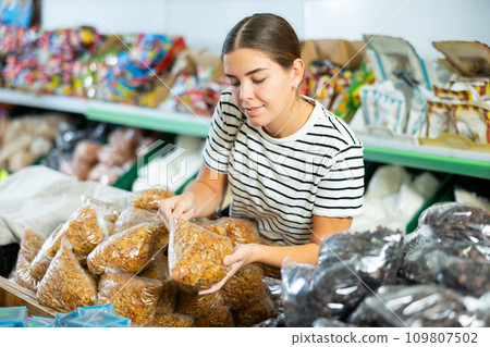 Young girl is in department of market with packaged products and is thinking about what to choose Young girl is in department of market with packaged products and is thinking about what to choose 109807502