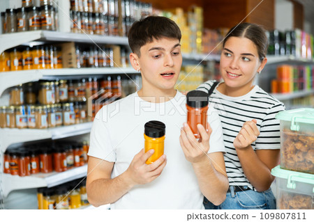 Cheerful young couple choosing spices in glass jars in supermarket 109807811