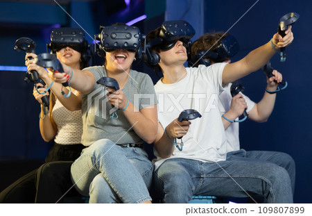 group of four friends wearing virtual reality glasses and with joysticks sit and play dynamic game group of four friends wearing virtual reality glasses and with joysticks sit and play dynamic game 109807899