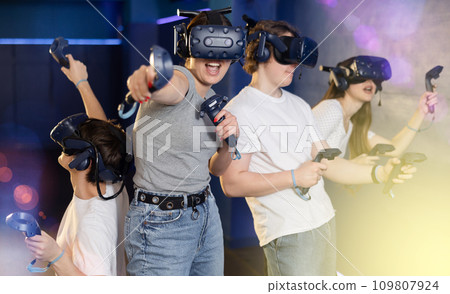 group of four friends wearing virtual reality glasses and with joysticks are playing dynamic game group of four friends wearing virtual reality glasses and with joysticks are playing dynamic game 109807924