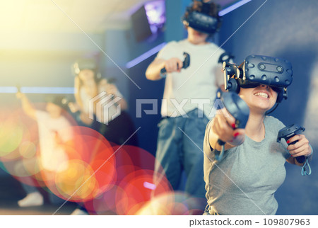 Young woman in VR glasses playing virtual game with handheld controllers Young woman in VR glasses playing virtual game with handheld controllers 109807963