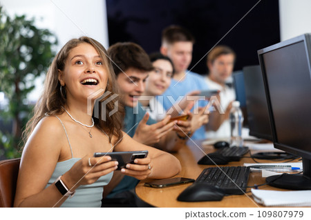 At computer class, young girl student sits with mobile phone and listens admiringly to teacher At computer class, young girl student sits with mobile phone and listens admiringly to teacher 109807979