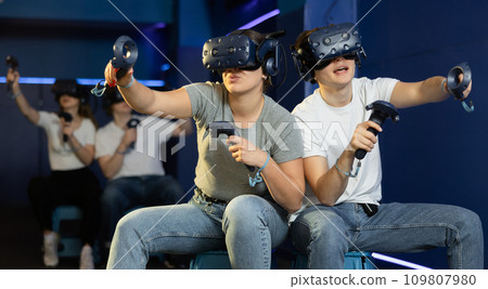 friends in helmets and with joysticks are sitting playing 3d action game. entertainment club friends in helmets and with joysticks are sitting playing 3d action game. entertainment club 109807980