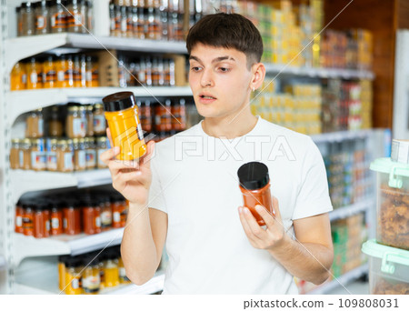 Guy chooses jars of spices in the grocery department of hypermarket 109808031