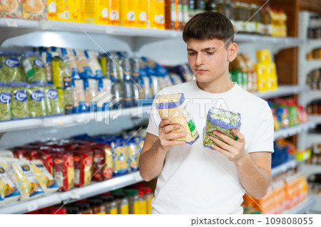 Guy carefully checks the information on product labels in hypermarket Guy carefully checks the information on product labels in hypermarket 109808055