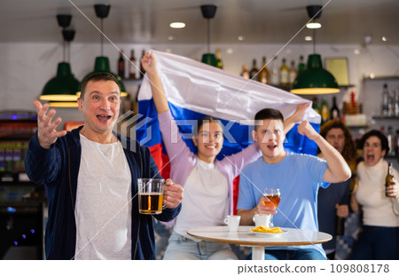 Happy friends of different ages drinking beer and celebrating the victory of the Russian team in night bar Happy friends of different ages drinking beer and celebrating the victory of the Russian team in night bar 109808178